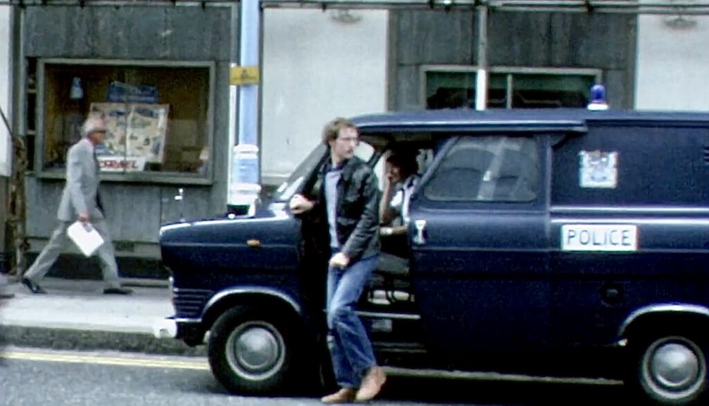 Jan stapt uit politiebusje als Engelse politie-inspecteur voor de deur van Scotland Yard in Londen. 